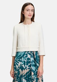 Biała krótka kurtka z fakturowanej tkaniny z frędzlami, z okrągłym dekoltem i rękawami do trzy czwarte.