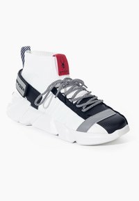 Sneaker alta bianca con accenti neri e grigi, lacci a righe, suola spessa e un'etichetta rossa con un logo di ragno sulla linguetta.