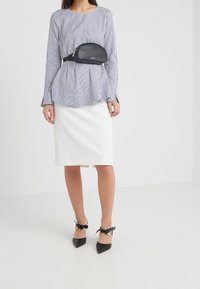 Černobílý pruhovaný dlouhý rukáv top s peplum designem, bílá tužková sukně a černé lodičky s špičatou špicí a mašlovými akcenty.