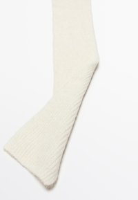 Sciarpa in lana lavorata a maglia di un morbido bianco sporco con una texture a coste, piegata diagonalmente su uno sfondo bianco semplice.