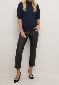 Marineblauwe pullover trui met korte, opbollende mouwen; gecombineerd met zwarte nep leren cropped broek en zwarte slingback hakken met gouden accenten.