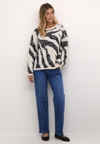 Pull en tricot épais avec un motif zèbre noir et blanc, col rond, manches longues. Associé à un jean bleu droit et des ballerines noires.