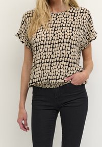 Blouse à manches courtes avec un motif abstrait beige et noir, confectionnée dans un tissu léger, présentant une coupe décontractée et un col rond.