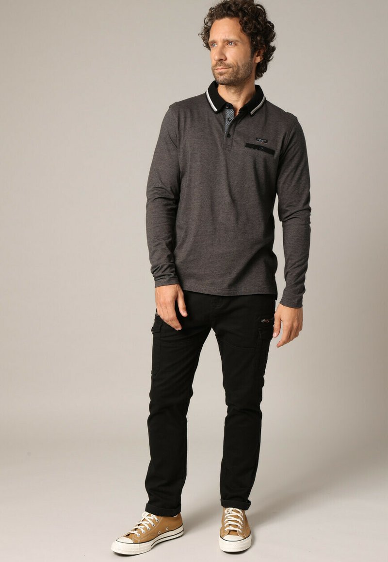 Langarmige charcoal polo met een contrasterende kraag, gecombineerd met zwarte cargo-broeken en tan sneakers. Voorzien van een borstzakdetail.