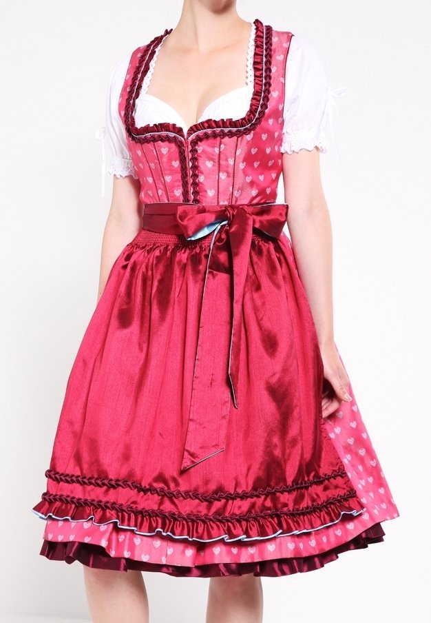 Femme portant une robe dirndl rouge traditionnelle avec motifs en forme de cœur, blouse blanche, jupe à volants et nœud en satin à la taille noué sur le côté.