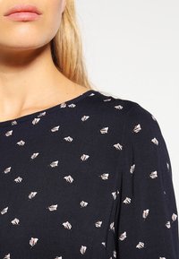 Blusa blu navy con piccoli motivi a foglia rosa chiaro sparsi. Collo rotondo e morbida texture del tessuto, che mette in risalto una vestibilità rilassata.