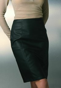 Zwarte leren kokerrok met een aansluitende vorm, zichtbare naden en een gladde textuur. Gecombineerd met een beige metallic lange mouwen top.