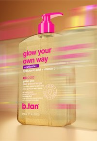 Clear golden shimmer gradual tan gel bottle with pink pump, labeled "glow your own way" with hyaluronic acid, vitamin C, vegan and cruelty-free.