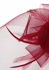 Roter Tüllhut mit zarten Schichten, der strukturierter Stoff und luftige Akzente aufweist, was ein voluminöses und komplexes Design schafft.