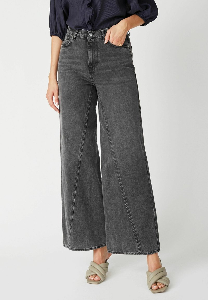 Jean en denim noir à larges jambes, dotés d'une taille haute et de poches latérales, agrémentés d'une finition texturée subtile.