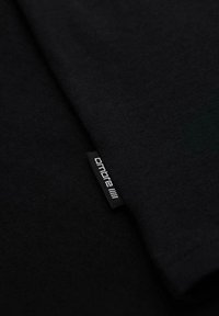 Nahaufnahme eines schwarzen Stoffs mit einem kleinen schwarzen Etikett mit der Aufschrift "ombre" in weißem Text entlang der Naht.