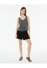 Camiseta sin mangas gris con un bolsillo, con un escote en forma de barco y un dobladillo fluido, combinada con pantalones cortos negros y sandalias negras.