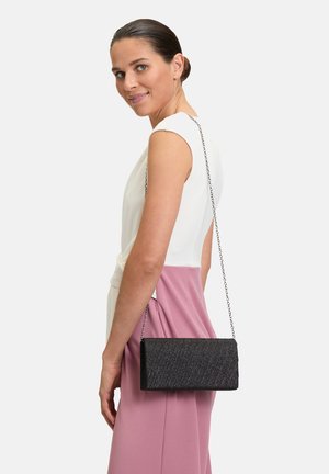 Borsa a tracolla nera testurizzata con forma rettangolare e catena, mostrata accanto a una persona che indossa un top bianco e una gonna rosa.