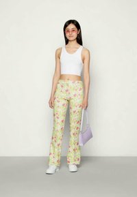 Calças justas de floral amarelo com flores cor-de-rosa, combinadas com um top cropped branco e ténis brancos, segurando uma mala lavanda.