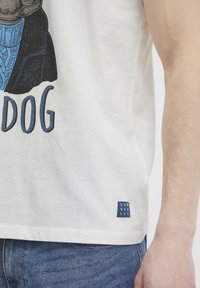 Hvid bomulds T-shirt med grafik af en hund og teksten "DOG" i blå. Har et lille blåt brandmærke ved sømmen.