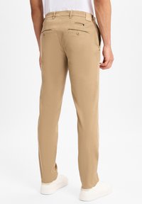 Pantaloni chino beige con vestibilità dritta. Presentano due tasche posteriori con bottoni e tasche laterali. Realizzati in un tessuto morbido e liscio.
