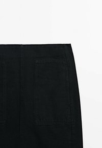 Jupe en denim noir avec taille haute, deux poches arrière et coutures visibles. Le tissu a une texture lisse et un design minimal.