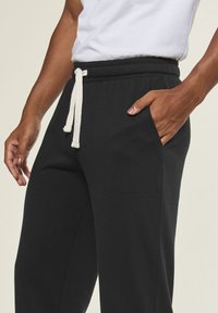 Black sweatpants made of soft cotton blend, featuring a drawstring waistband, side pockets, and smooth texture.