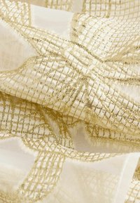 Tessuto setoso con una base di un leggero avorio, caratterizzato da un motivo a griglia dorata e una lucentezza sottile. La texture spiegazzata mette in risalto dettagli intricati.