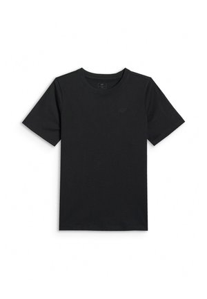Un jeune garçon se tient debout, portant un t-shirt noir, un sweat-shirt bleu clair posé sur les épaules, un pantalon cargo marron et des baskets noires et blanches.