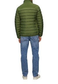 Grüne Daunenjacke mit hohem Kragen, ge quiltetem Design und glatter Textur, kombiniert mit hellblauen Jeans und weißen Sneakers.