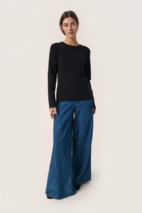 Pulover negru cu mânecă lungă, asortat cu blugi albaștri cu pantaloni largi. Puloverul are un gât rotund și o textură fină.