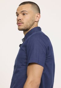 Chemise à manches courtes bleu marine en tissu texturé avec un col boutonné et des boutons sur le devant. Présente une coupe décontractée et une finition lisse.