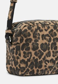 Zamszowa torba na ramię w cętki lamparta z czarnym skórzanym paskiem, zamkiem błyskawicznym i złotym tłoczonym logo na przodzie. Miękka tekstura i kompaktowy kształt.