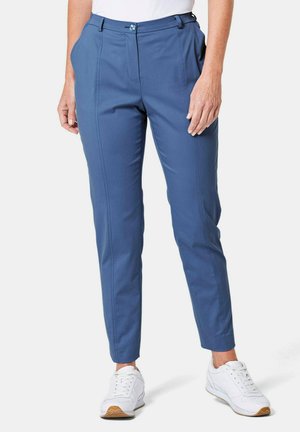 Pantalon bleu slim-fit composé d'un tissu lisse avec une taille plate, des poches latérales et une fermeture à un bouton. Associé à des baskets blanches.