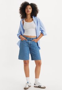 Lyseblå denimshorts, midt på låret, kombinert med en hvit tanktop og en åpen, lys blå skjorte med knapper. Hvite og grå joggesko.