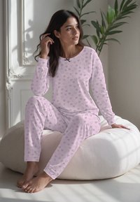 Vaaleanpunainen pyjama, jossa on pitkät hihat ja housut, joissa on sydänkuvio eri harmaan sävyissä. Pehmeää kangasta, jossa on pyöreä pääntie ja pieni nauhakoriste.