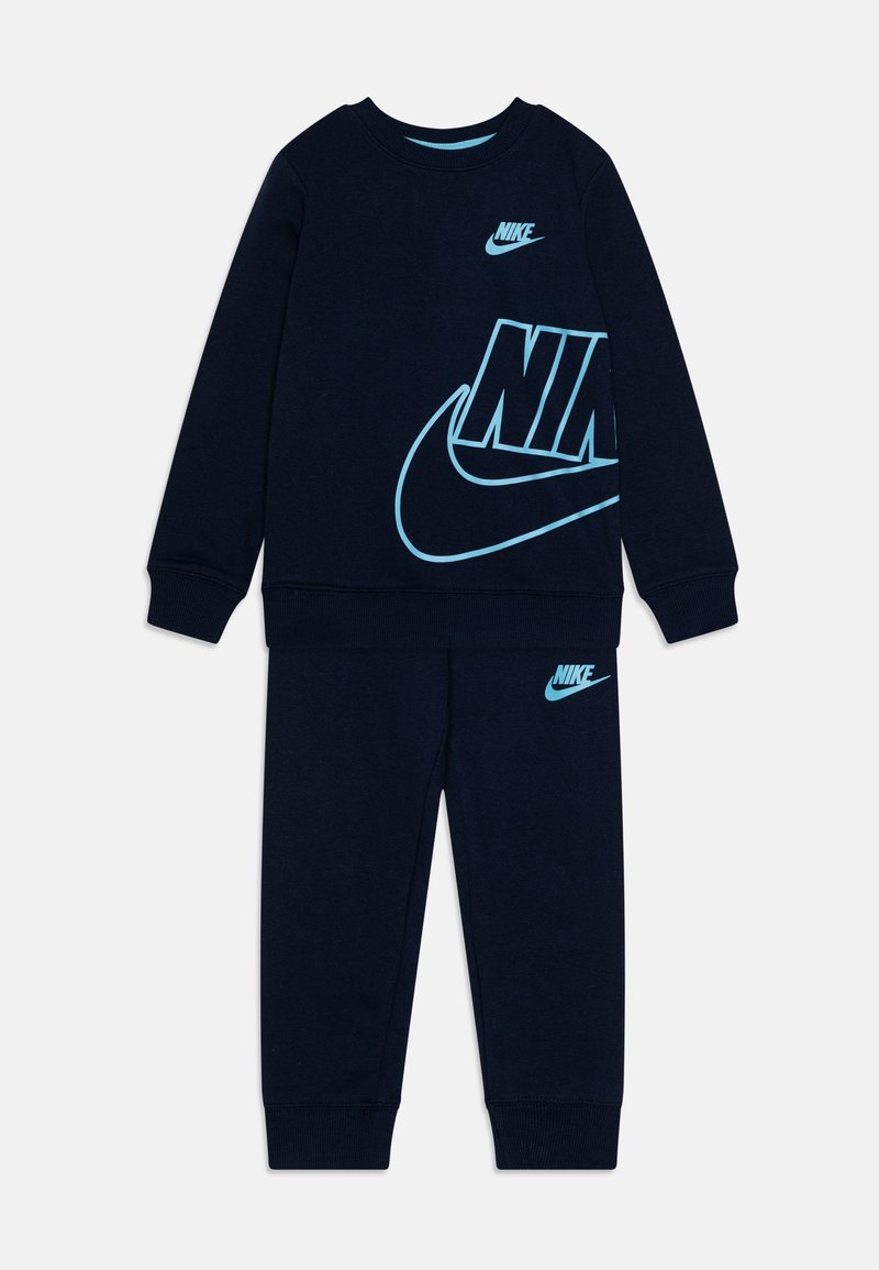 Chándal de forro polar azul marino con el logo de Nike en azul claro. El sudadera cuenta con un gráfico grande; los pantalones tienen un logo más pequeño. Textura suave, puños elásticos.