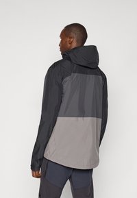 Veste imperméable en noir et gris. Dotée d'une capuche, d'un design en blocs de couleur et d'une texture lisse, avec une coupe décontractée et des manches longues.