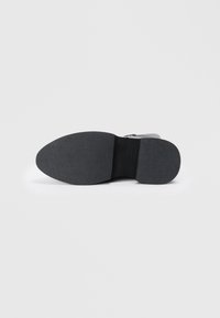 Melnā gumijas zole ar struktūru, nedaudz ieliektu formu. Iezīmējas ar gludu ādas virsējo daļu un rāvējslēdzēja detaļu.