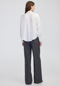 Weiß gestreiftes Langarmhemd mit einer Rückenpasse und weicher Textur, kombiniert mit dunkelgrauen weiten Hosen.