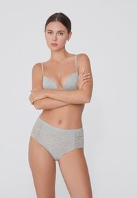 Světle šedá podprsenka s hlubokým výstřihem a tenkými ramínky, doplněná o odpovídající vysoké kalhotky s krajkovými bočními panely.