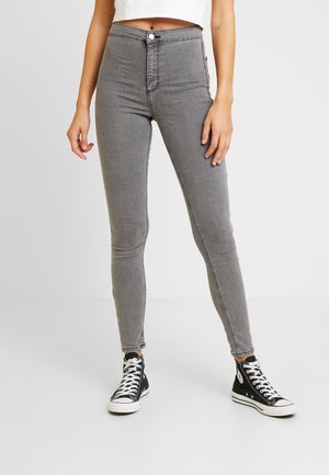 Jeans skinny gris taille haute avec fermeture à bouton, cinq poches et coutures contrastées, associés à des baskets montantes noires.