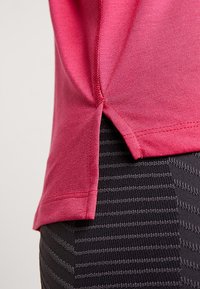 Rosa kortärmad skjorta med sidospjälor, slät textur och rundad fåll, ihop med svarta leggings med randigt mönster.