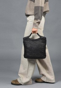 Zwarte geweven handtas met een gestructureerd ruitpatroon, een ronde bovenkant en twee korte handvatten. Het materiaal lijkt stevig en duurzaam.