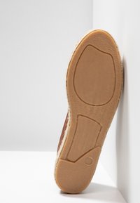 Semelle d'une chaussure marron avec une semelle en caoutchouc texturée et le numéro de taille 37 visible, positionnée à la verticale contre des surfaces blanches.