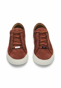 Brown suede sneakers with lace-up design, white rubber sole, visible logo accents on tongue, and textured fabric detail.