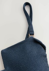 Sac en tissu côtelé bleu marine avec une surface texturée, doté d'une sangle à boucle et d'un accent métallique au point d'attache.