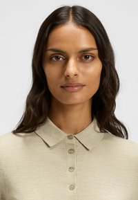 Ljus beige pikétröja med krage, med fem knappar framtill, tillverkad av ett slätt, strukturerat tyg.