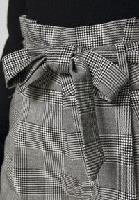 Black and white checkered fabric featuring a bow detail at the waist, with a textured surface and varying pattern sizes.