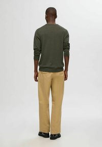 Mörkgrön tröja med ribbade muddar och fåll, i kombination med beige byxor och svarta skor. Designen är enkel och klassisk i formen.