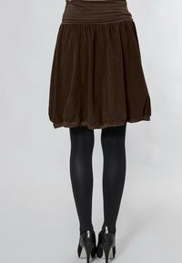 Brauer Samtrock mit einem gerafften Design, tailliertem Bund und einem Saum oberhalb des Oberschenkels. Kombiniert mit schwarzen Strumpfhosen und High Heels.