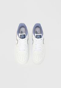 Fehér Nike Air Force 1 tornacipők, sima bőr felsőrésszel, perforált orr-résszel, kontrasztos szürke sarokkal és fehér cipőfűzővel.