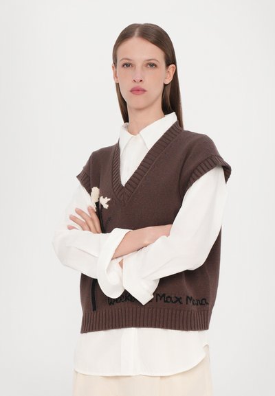 Brauner Strickwesten mit V-Ausschnitt, kurzen Ärmeln und besticktem Blumenmuster. Über einem weißen Hemd mit Kragen getragen, mit geripptem Saum.