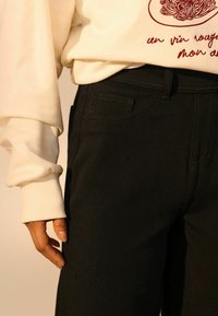 Pantalons en denim noir avec une coupe ajustée, une poche avant et des détails de couture, associés à un sweat-shirt crème avec des poignets côtelés et un imprimé graphique.