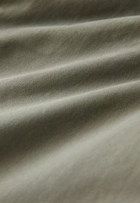 Cotton fabric in an olive green color with a smooth texture, displaying diagonal ribbing and gentle folds throughout.